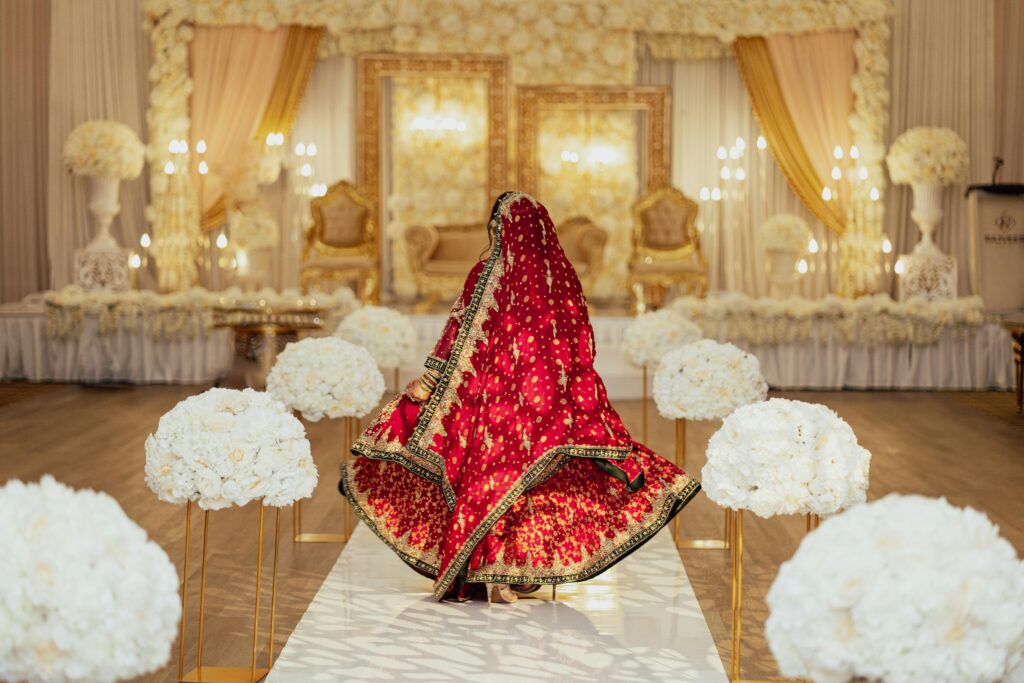 Back view of a bride in a red lehenga at a lavish wedding venue.