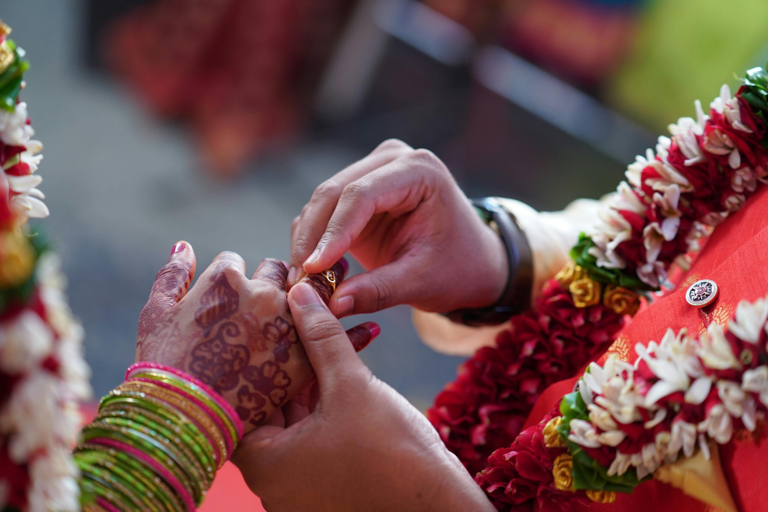 Close-up shot of an Indian wedding ring exchange with henna and floral decorations.