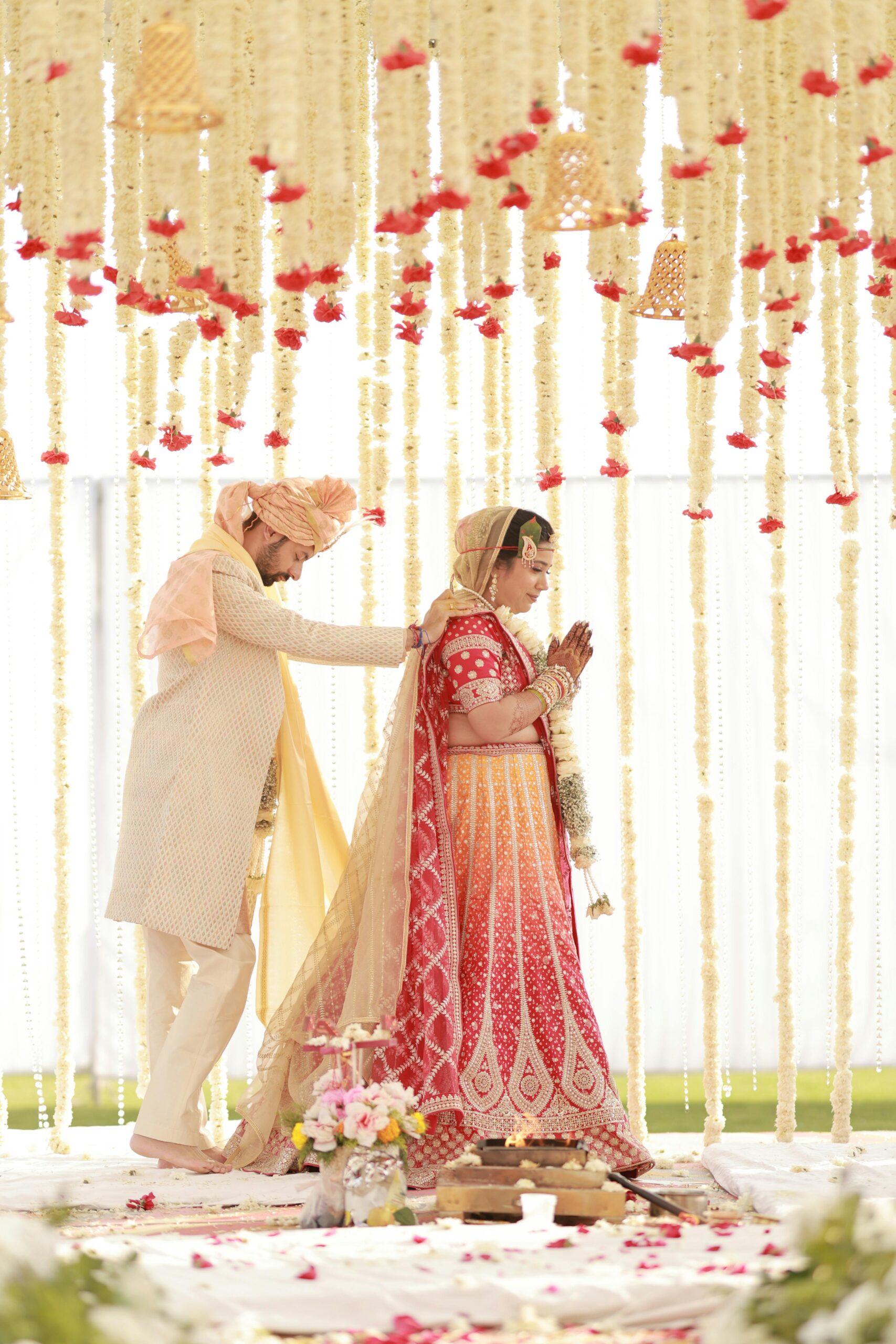Bride and groom performing a traditional Indian wedding ceremony under decorative floral arrangements.